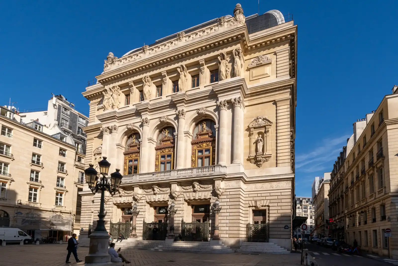La façade sculptée de l'Opéra Comique se dresse majestueusement sous un ciel bleu dégagé.