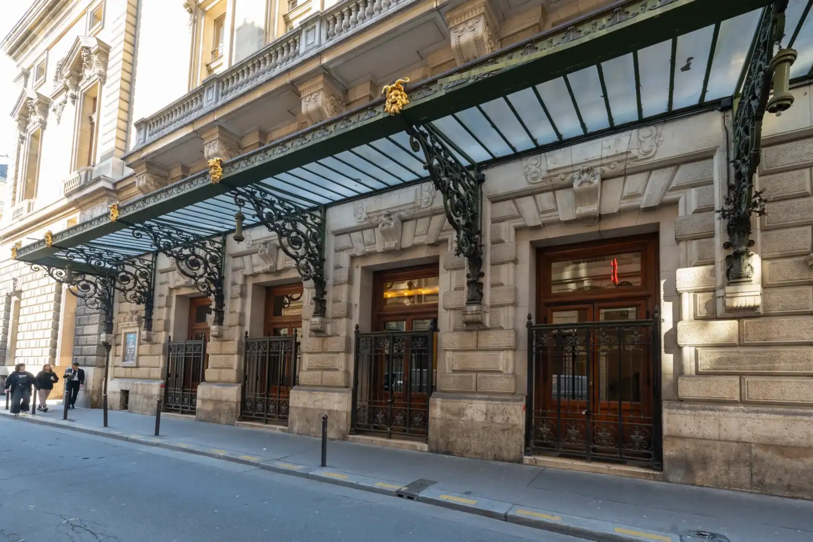 La façade en pierre de l'Opéra Comique présente une marquise en fer forgé ornée.