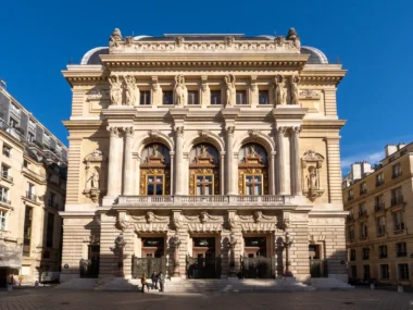 La façade monumentale de l'Opéra Comique à Paris sous un ciel bleu éclatant.