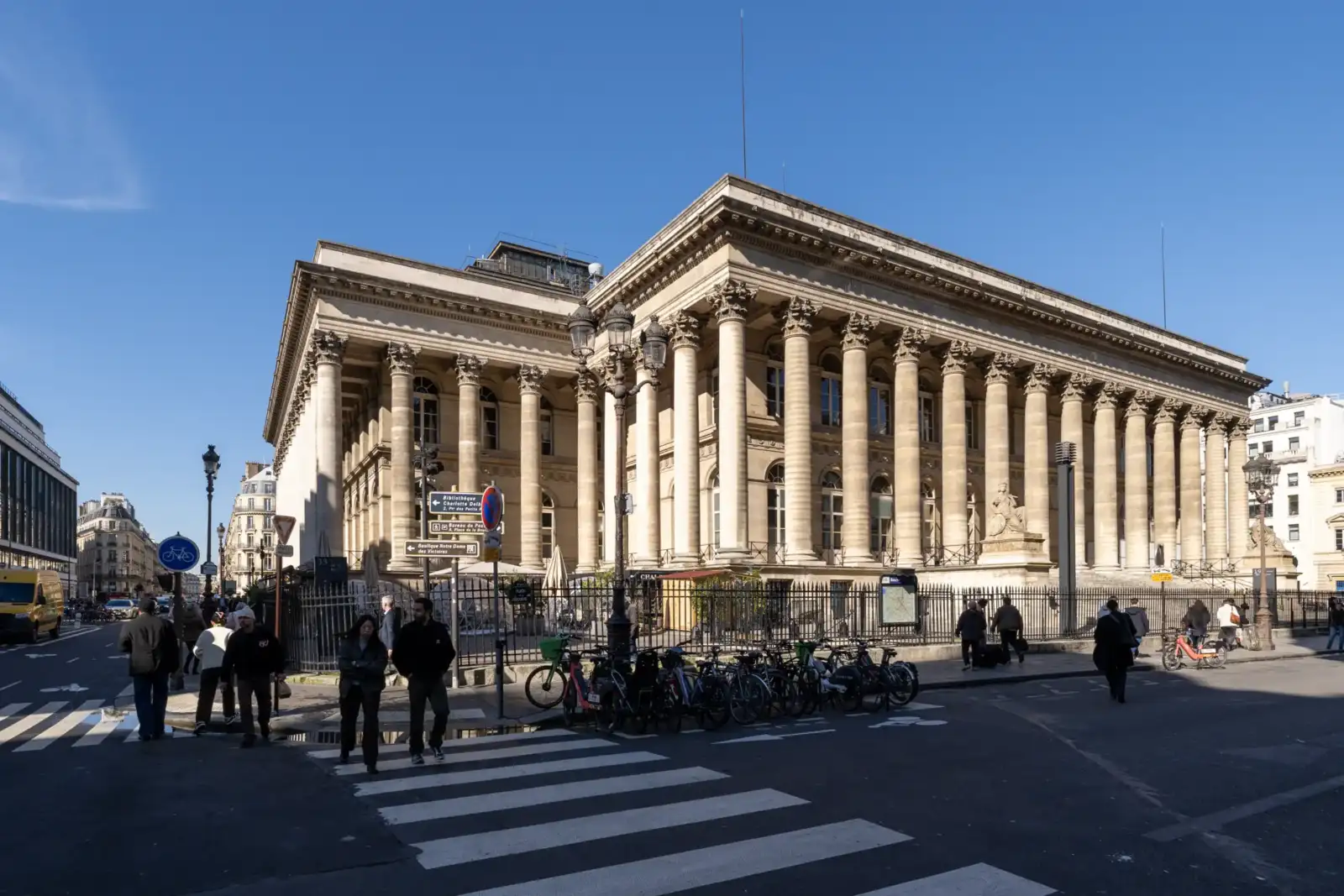 Vue extérieure de face de la façade néoclassique du Palais Brongniart sous un ciel bleu.