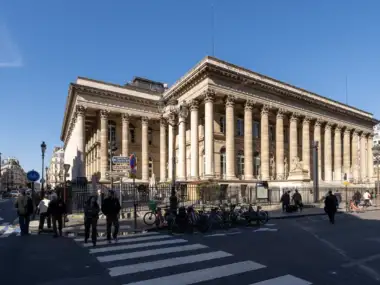 Vue extérieure de face de la façade néoclassique du Palais Brongniart sous un ciel bleu.