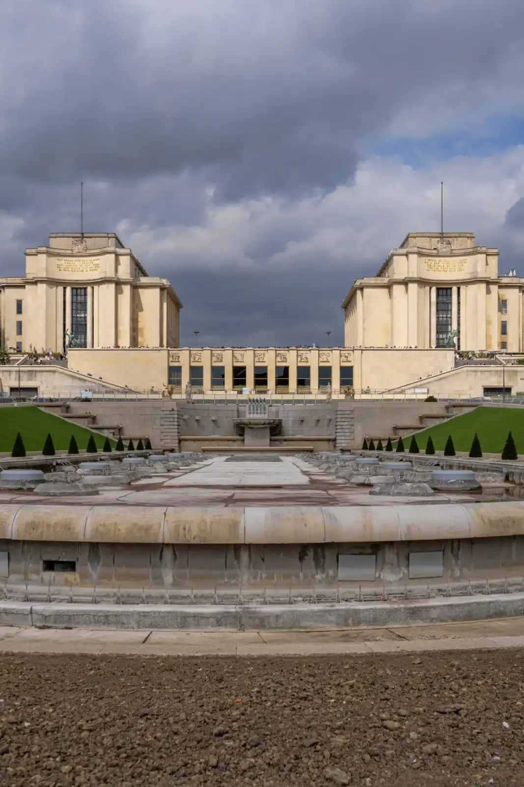 Vue frontale du palais de Chaillot et ses fontaines sous un ciel nuageux.