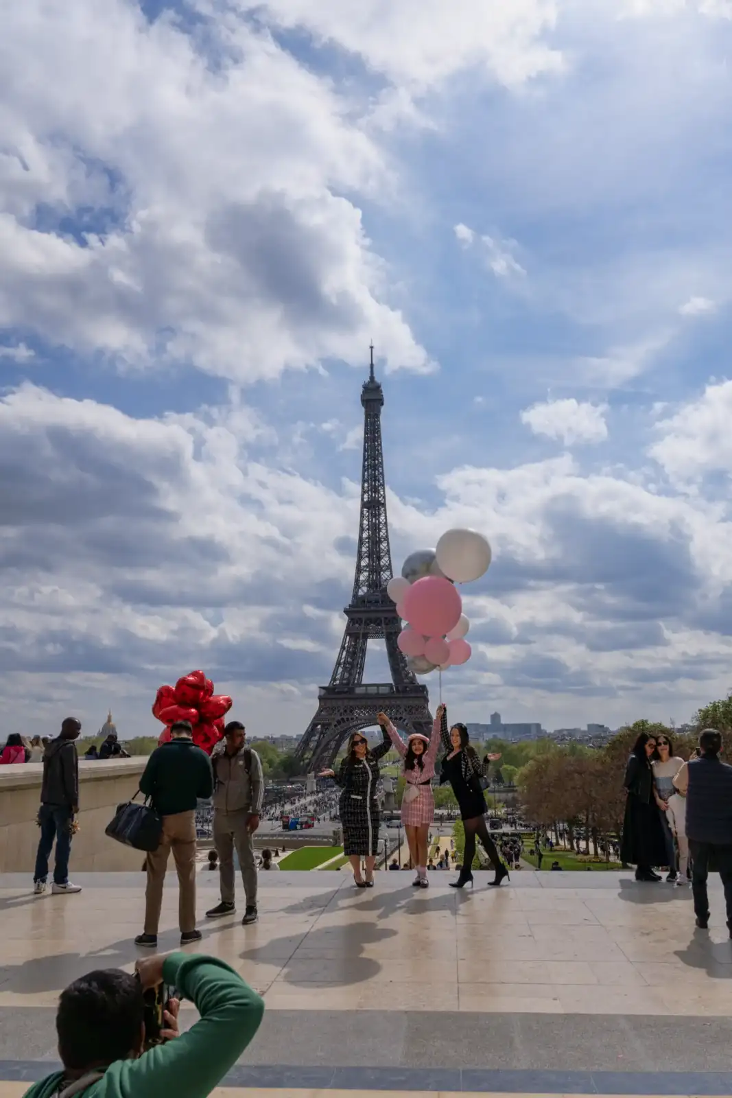 Trois femmes tenant des ballons posent joyeusement devant la tour Eiffel au Trocadéro.