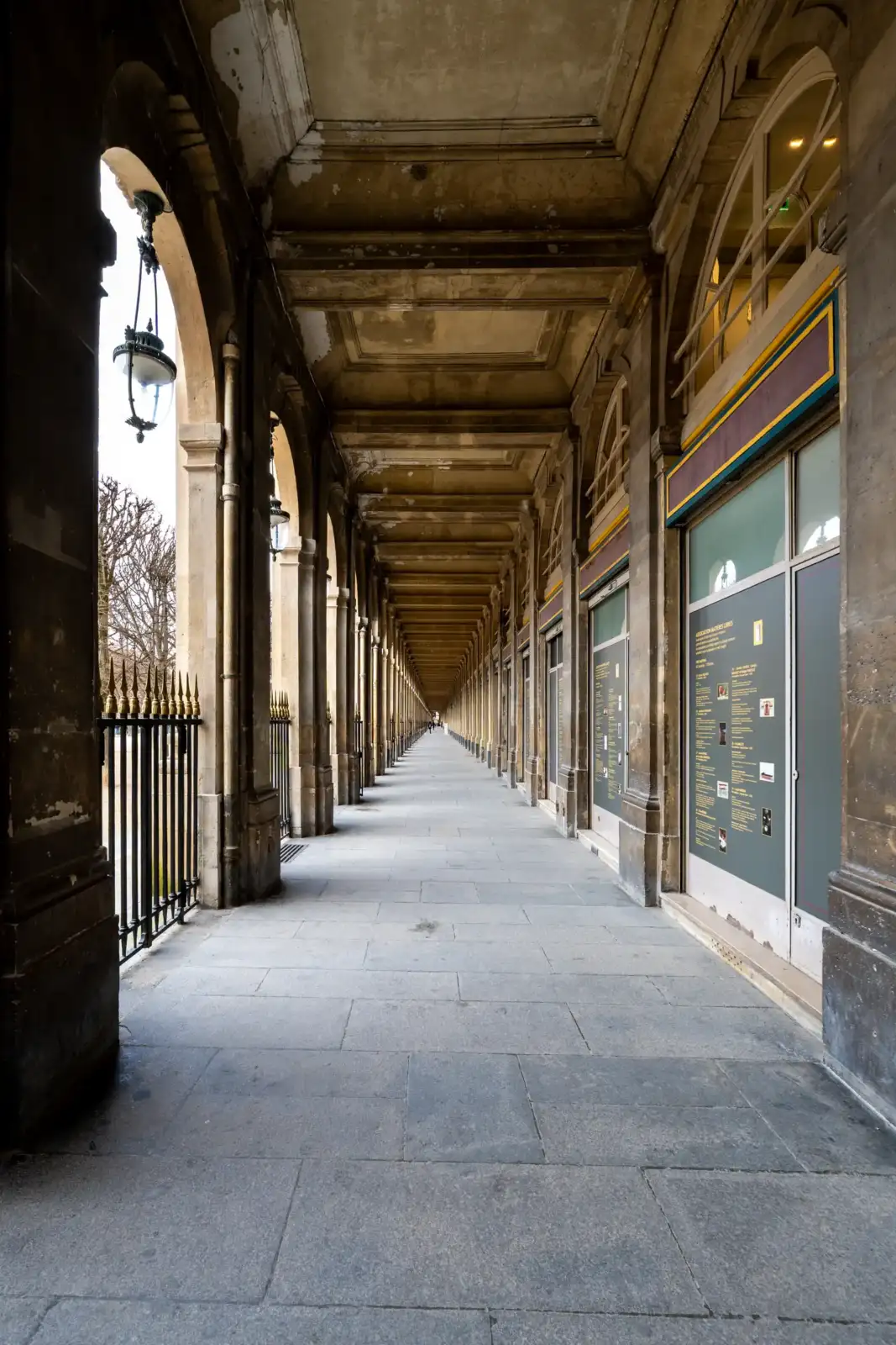 Une longue galerie couverte aux arcades classiques borde les jardins du Palais Royal parisien.