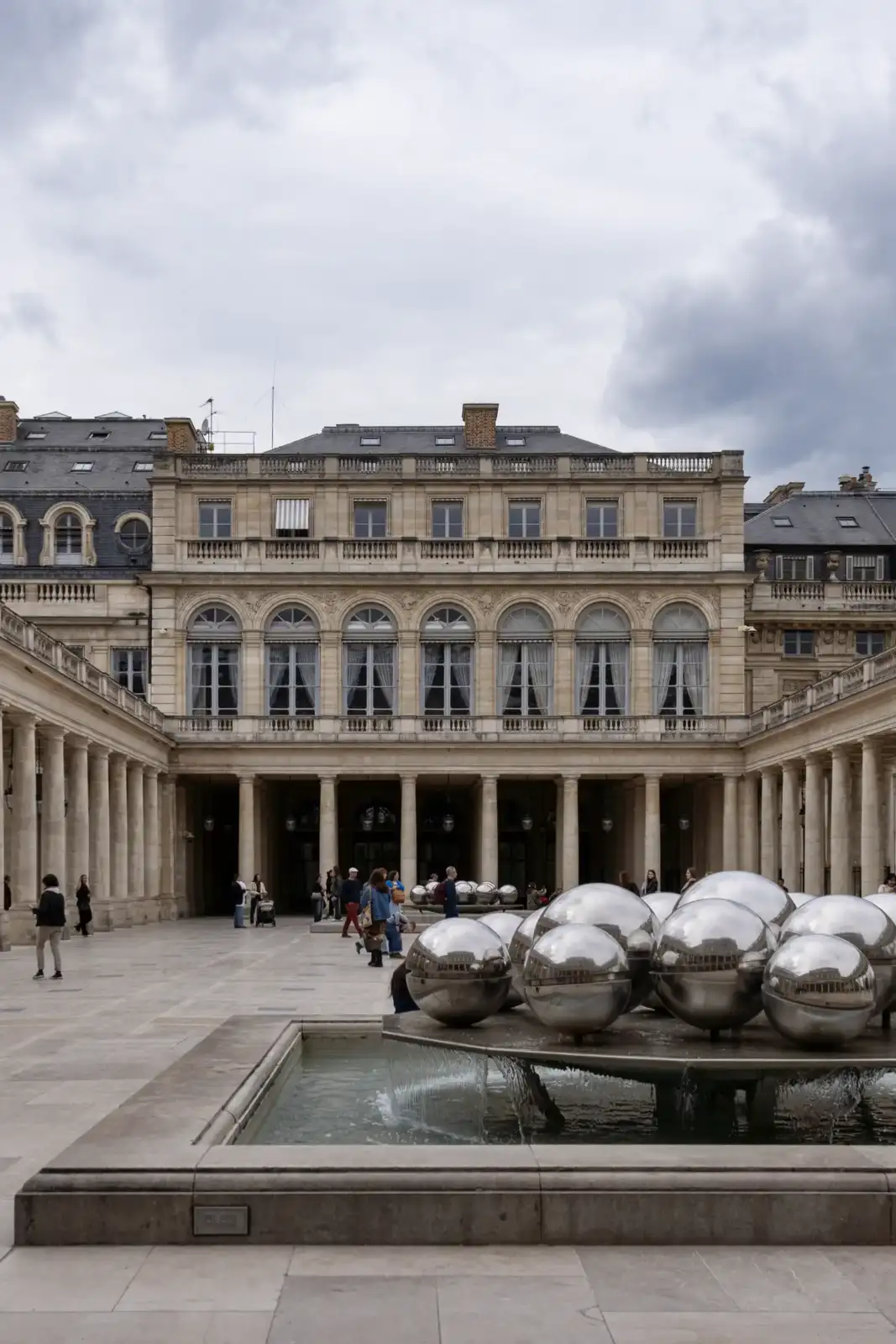 Fontaine aux sphères métalliques devant la façade classique du Palais Royal à Paris.