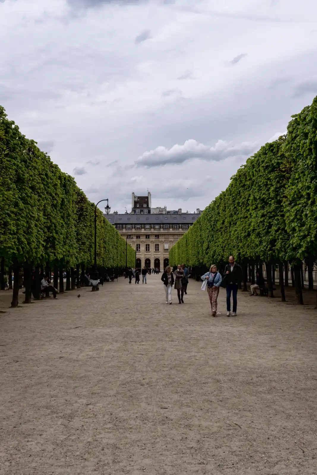 Des promeneurs marchent dans l'allée centrale bordée d'arbres du jardin du Palais Royal.
