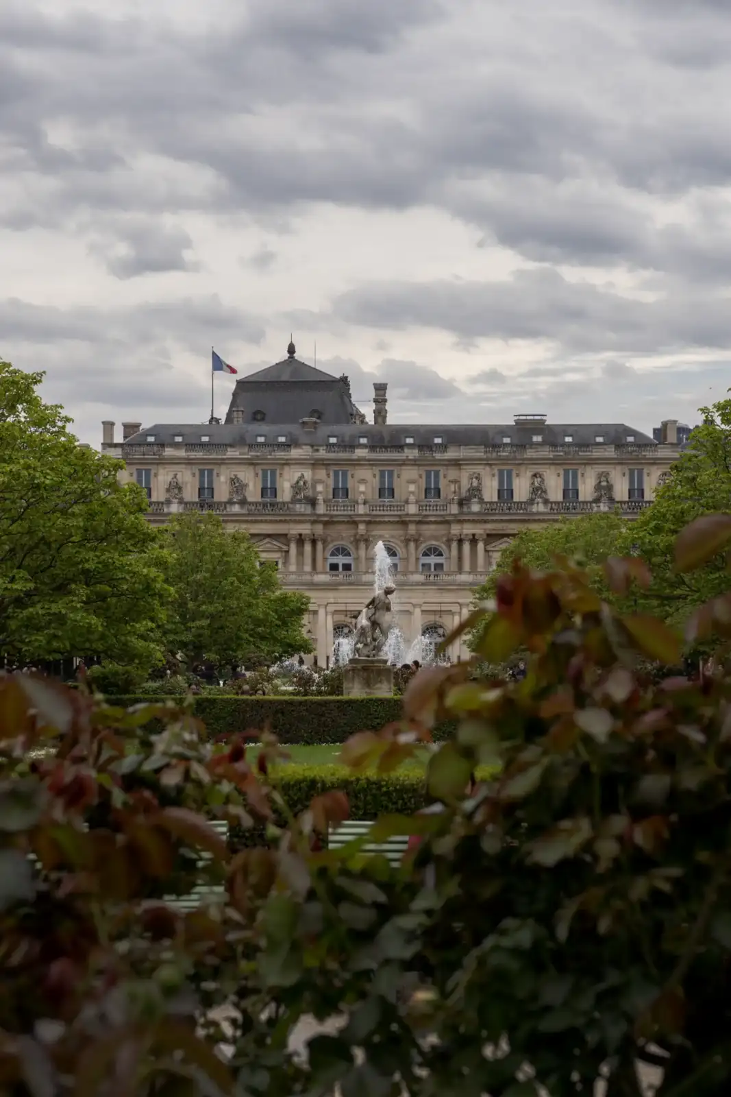 Une fontaine orne les jardins verdoyants devant la façade classique du Palais Royal parisien.