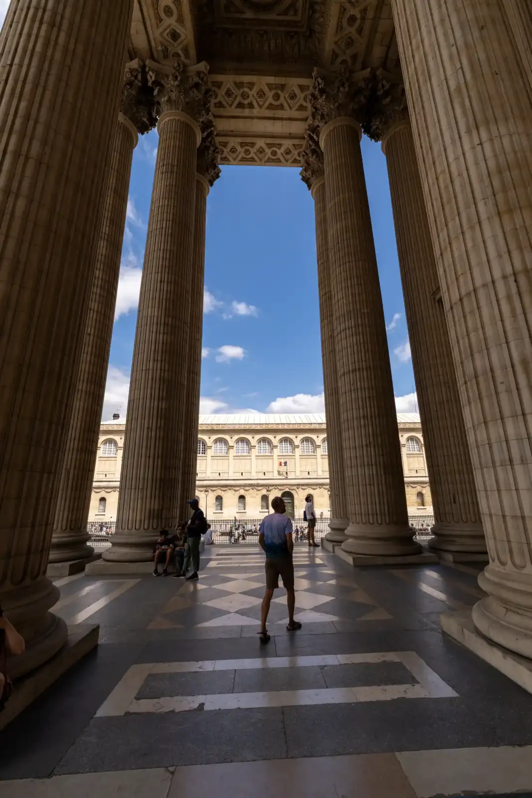 De grandes colonnes encadrent la façade du Panthéon de Paris sous un ciel bleu.