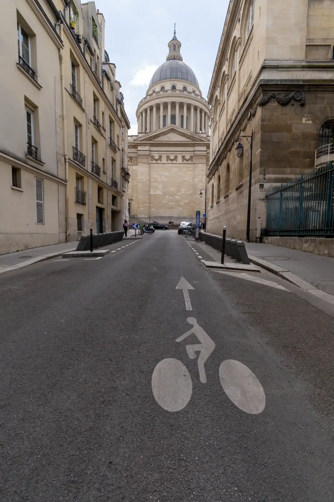 Une rue parisienne avec un pictogramme de vélo, encadrée par des immeuteurs anciens et le Panthéon.