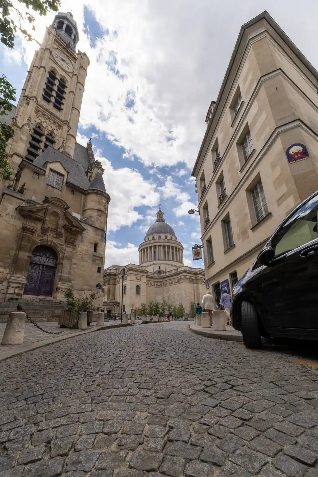 Vue en contre-plongée d'une rue pavée parisienne menant au Panthéon sous un ciel nuageux.