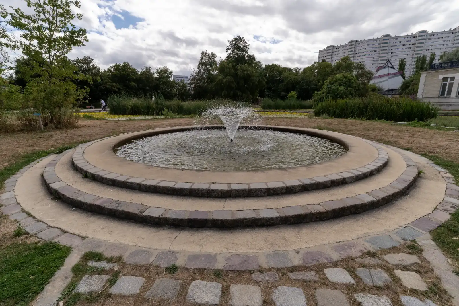 Une fontaine circulaire à jets d eau se trouve au milieu du parc parisien.