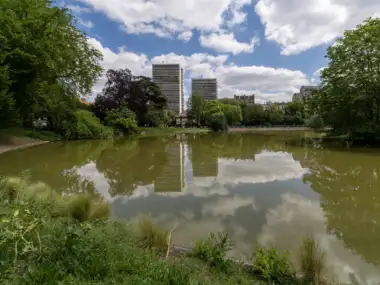 Le lac du parc Montsouris reflète des immeubles parisiens sous un ciel nuageux.