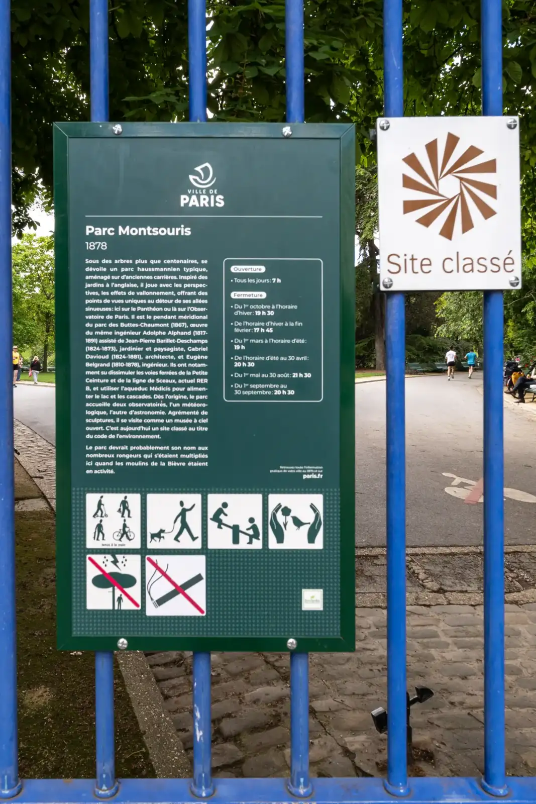 Panneau d'information vert devant l'entrée arborée du parc Montsouris à Paris 14e arrondissement.