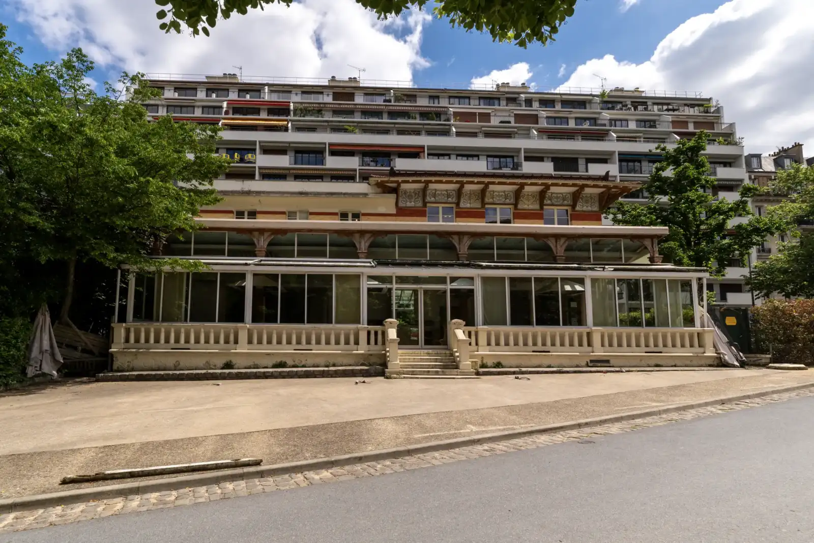 Un bâtiment ancien avec véranda se dresse devant un grand immeuble moderne au parc Montsouris.