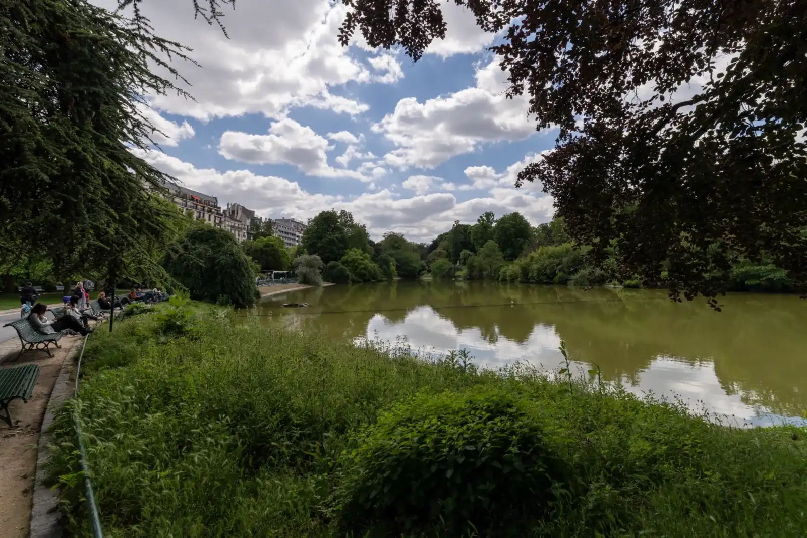 Vue panoramique du lac au parc Montsouris entouré d'arbres sous un ciel nuageux.