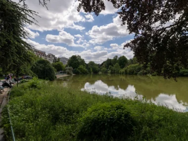 Vue panoramique du lac au parc Montsouris entouré d'arbres sous un ciel nuageux.