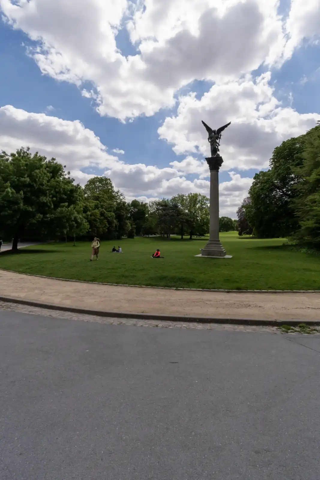 Une statue ailée trône au milieu d'une pelouse verdoyante dans le parc Montsouris ensoleillé.