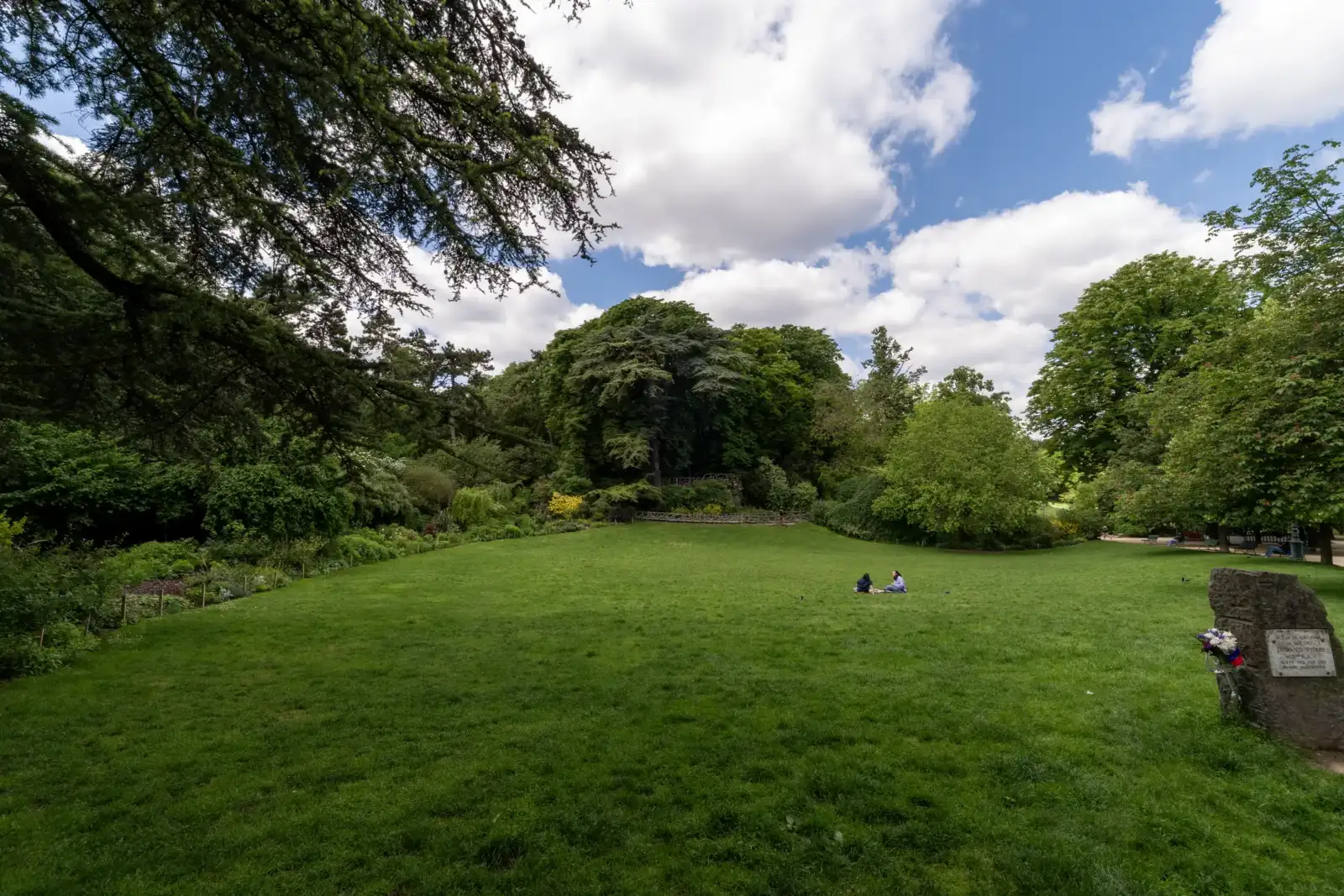 Deux personnes sont assises sur la grande pelouse verdoyante du parc Montsouris à Paris.