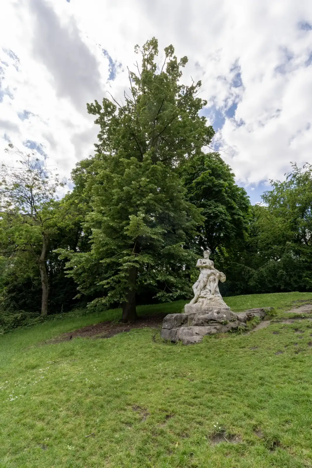 Une statue en pierre trône sur une pelouse verdoyante au parc Montsouris à Paris.