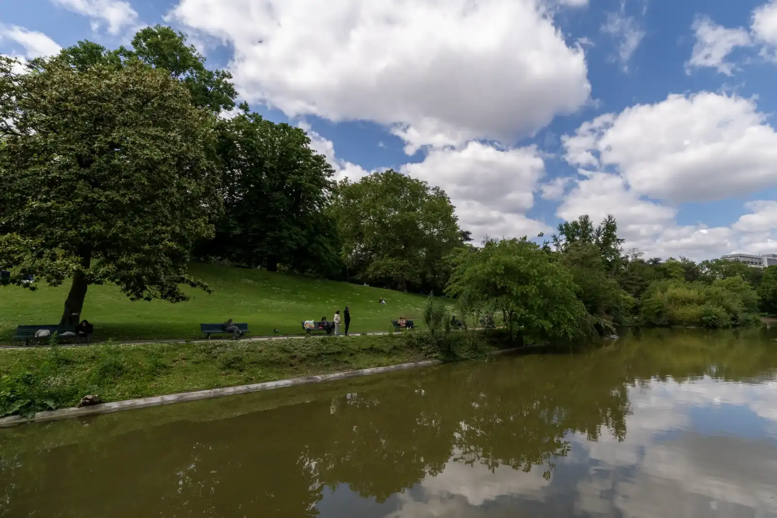 Des personnes se détendent sur des bancs au bord du lac au parc Montsouris.