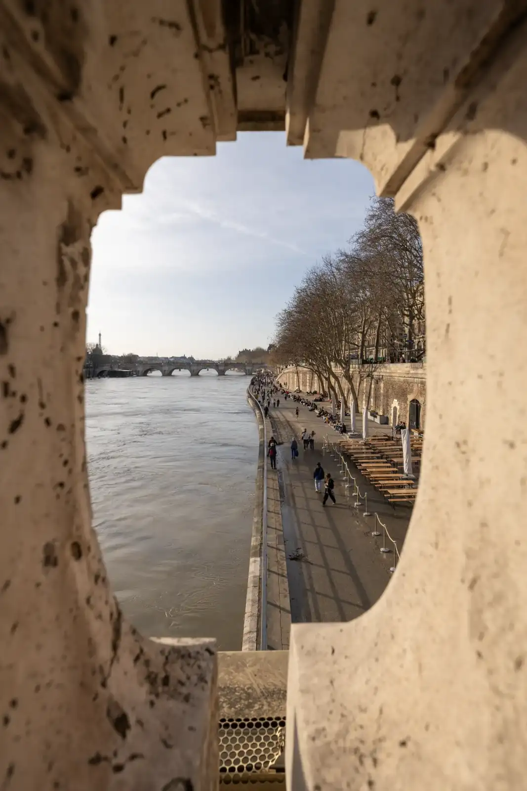 Vue encadrée des quais de Seine à Paris avec des promeneurs et des terrasses.