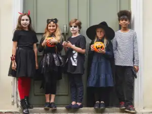 Cinq enfants déguisés pour Halloween posent devant une porte verte avec des seaux citrouilles.