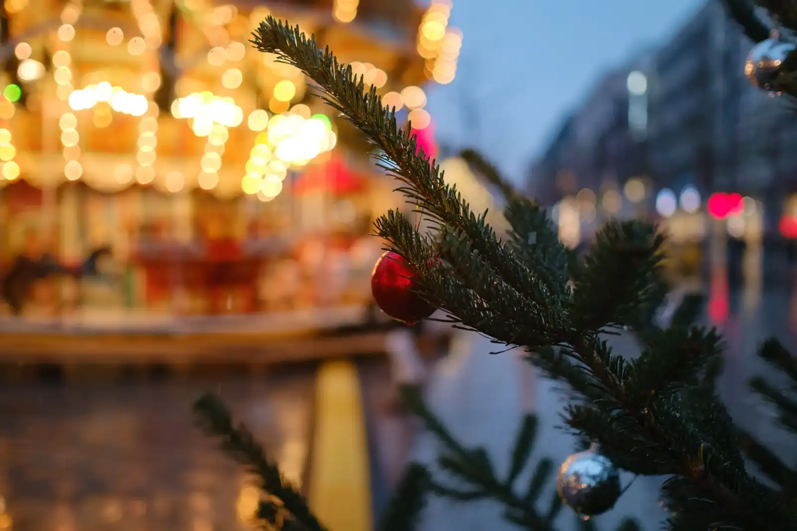 Une branche de sapin décorée avec des boules devant un manège illuminé à Paris.