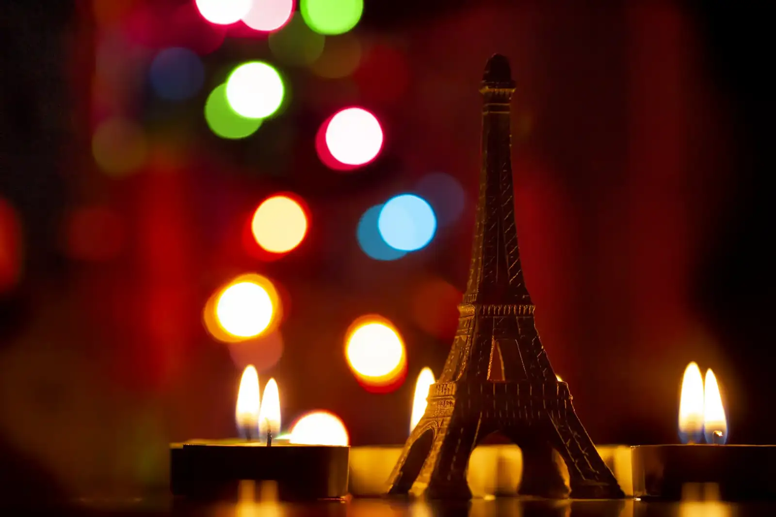 Une figurine de la tour Eiffel éclairée par des bougies devant des guirlandes lumineuses.