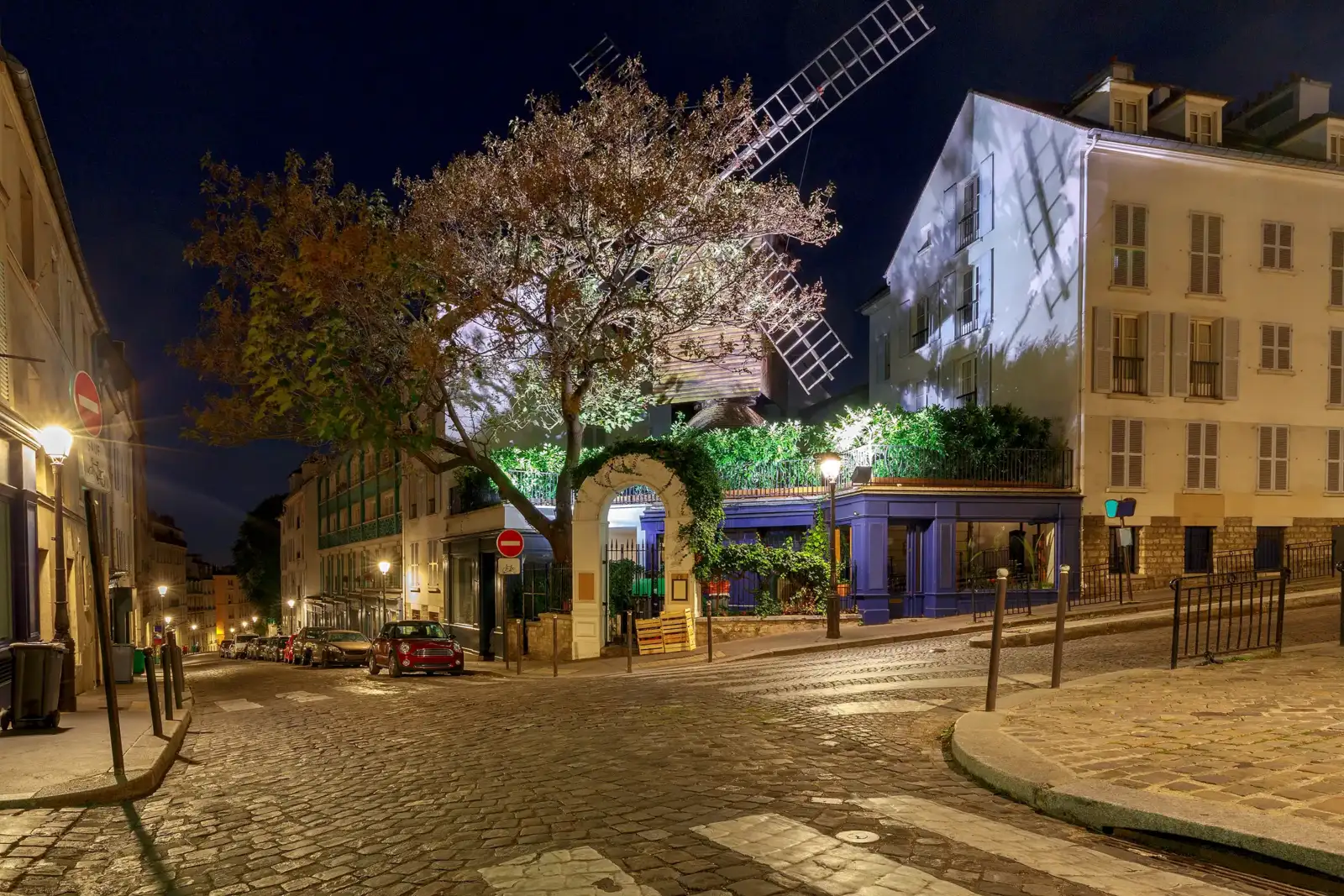 Un vieux moulin de Paris illuminé domine une rue pavée et calme la nuit.