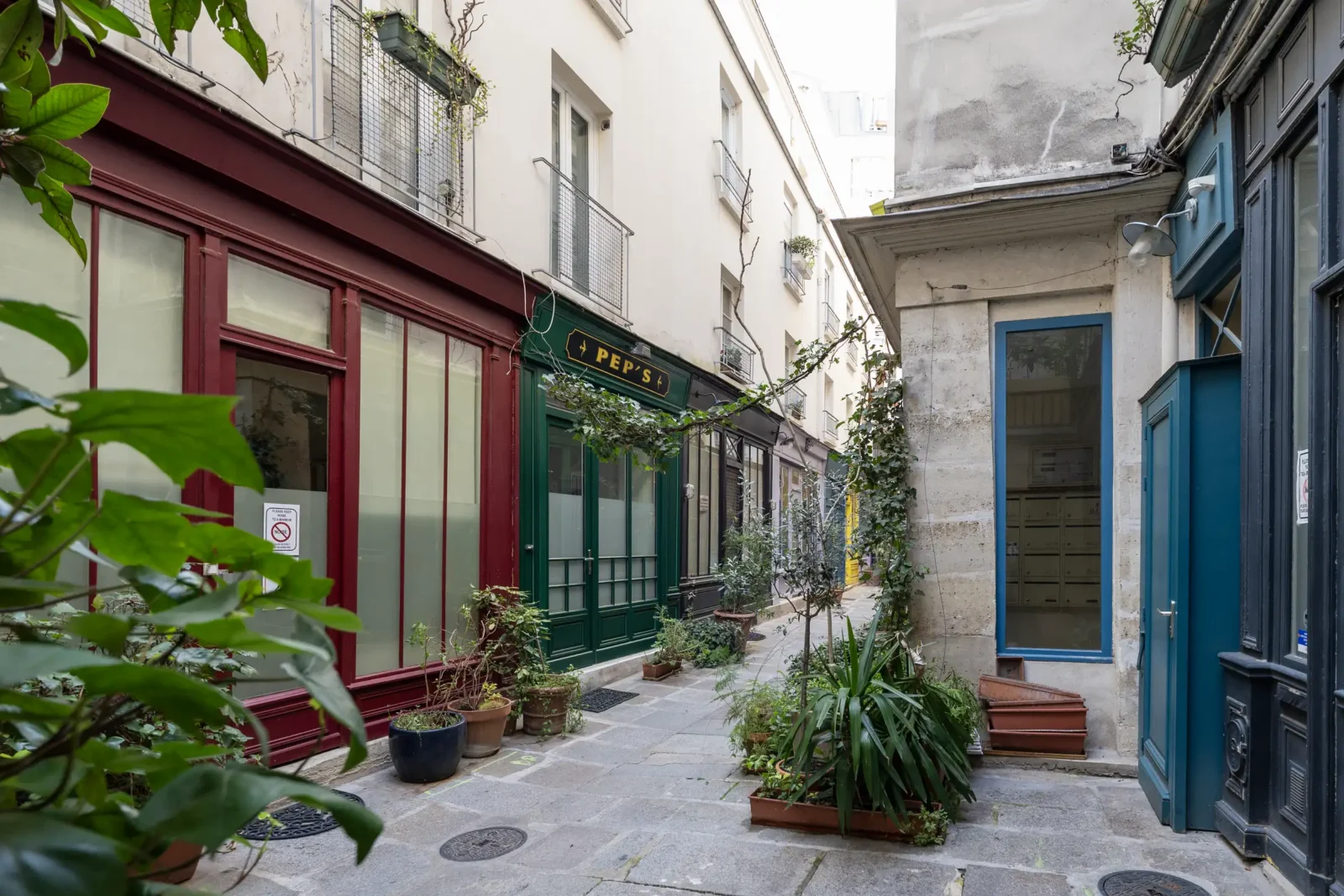 Une ruelle pavée et fleurie du Passage de l'Ancre à Paris avec des devantures colorées.