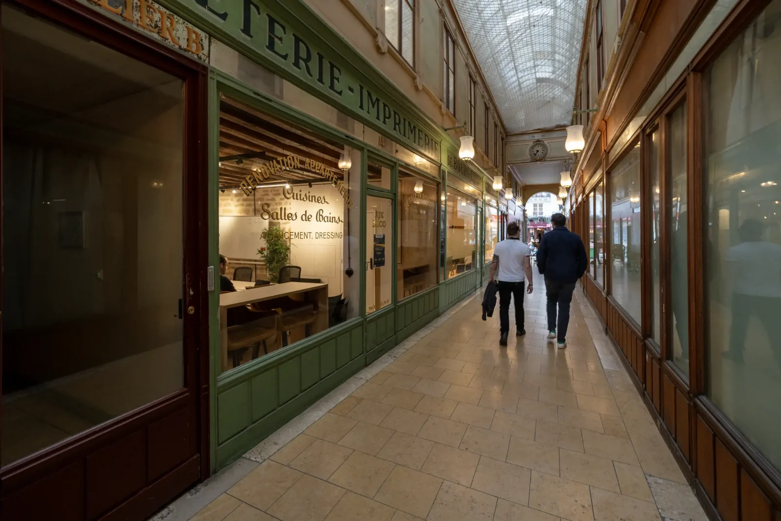 Deux hommes marchent dans le passage couvert historique du Bourg-l'Abbé à Paris.