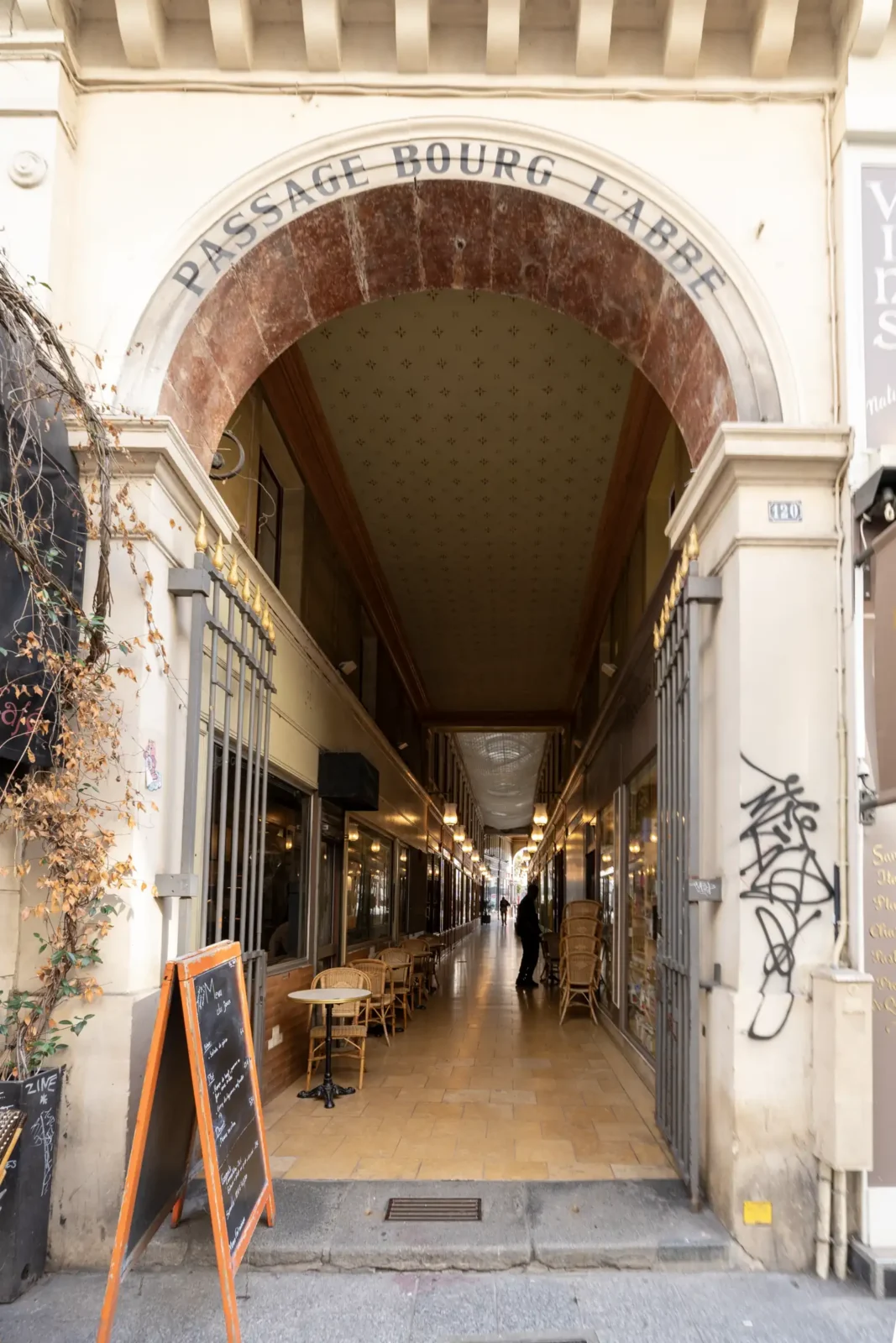 L'entrée voûtée du Passage Bourg l'Abbé à Paris avec ses chaises de terrasse alignées.
