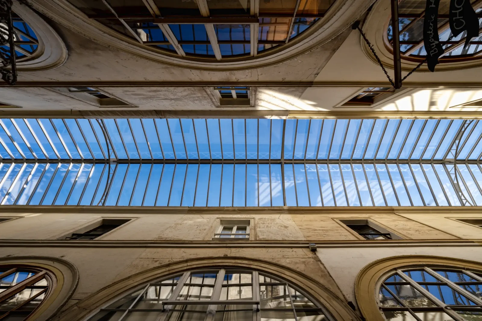 Vue en contre-plongée de la verrière historique du Passage Choiseul sous un ciel bleu.