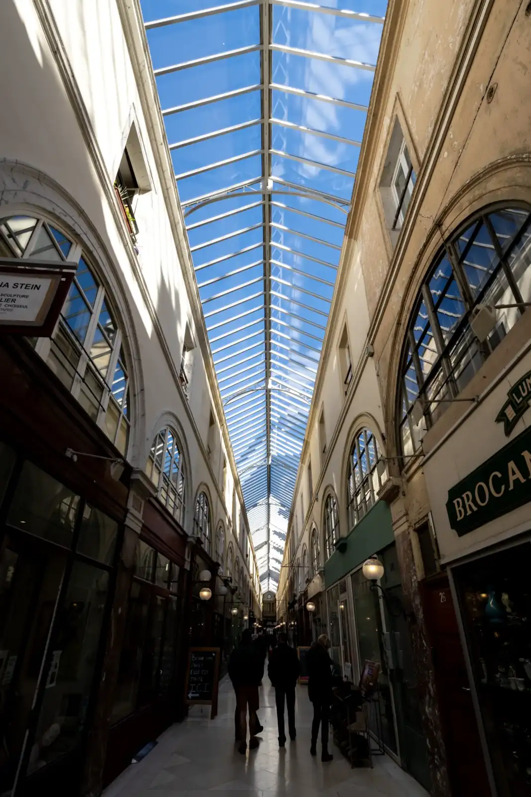 Vue en contre-plongée du Passage Choiseul avec sa verrière lumineuse surplombant les boutiques anciennes.