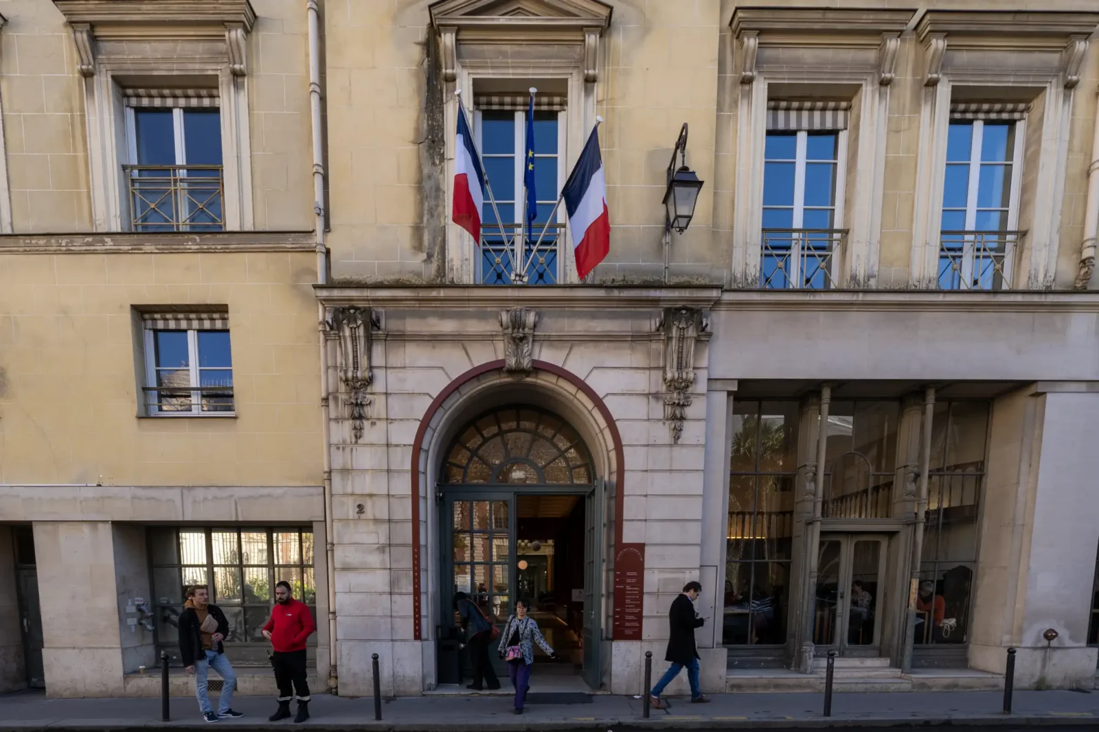 Façade classique du Passage Colbert à Paris avec des drapeaux français et européens flottant.