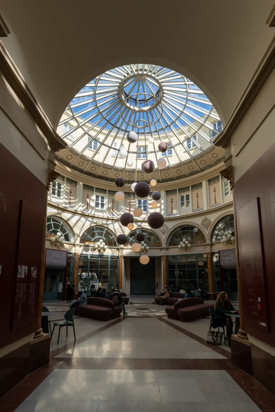 La verrière circulaire du Passage Colbert illumine un hall élégant avec des suspensions sphériques.