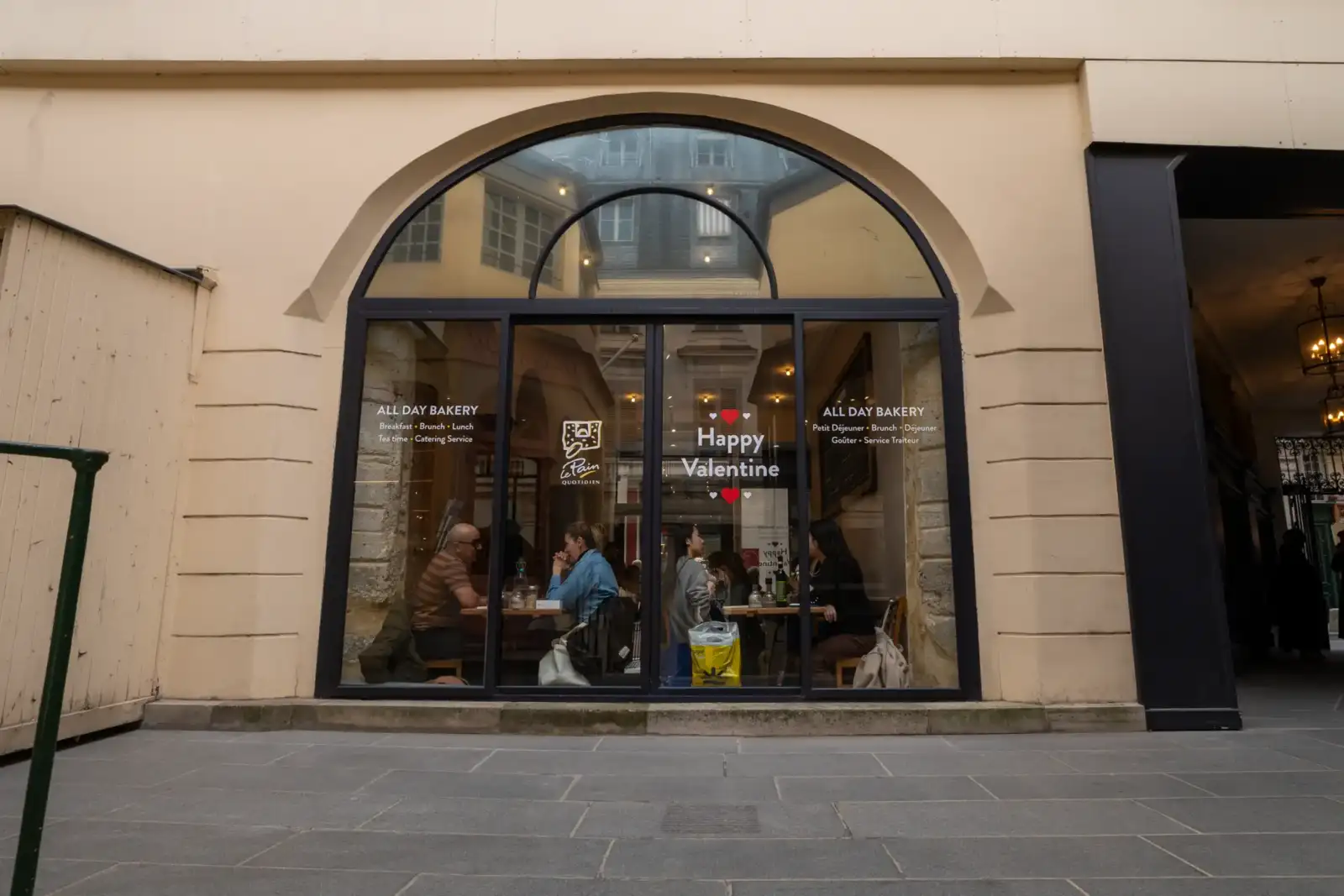 La façade vitrée d'une boulangerie parisienne avec des clients attablés à l'intérieur.