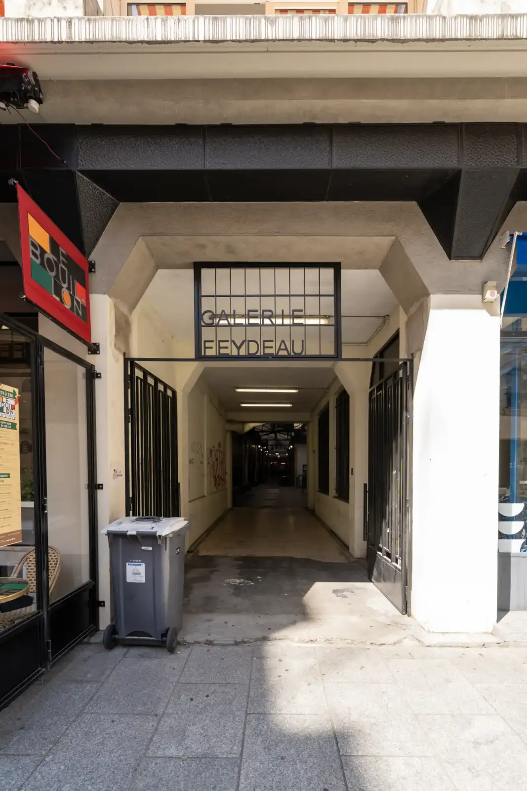 Vue de l'entrée de la Galerie Feydeau à Paris, avec une enseigne noire et une poubelle grise.