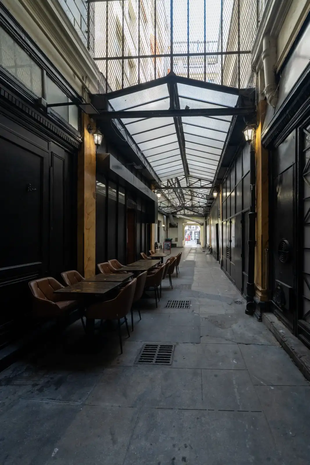 Vue intérieure du Passage Feydeau à Paris, avec des tables en terrasse sous une verrière.