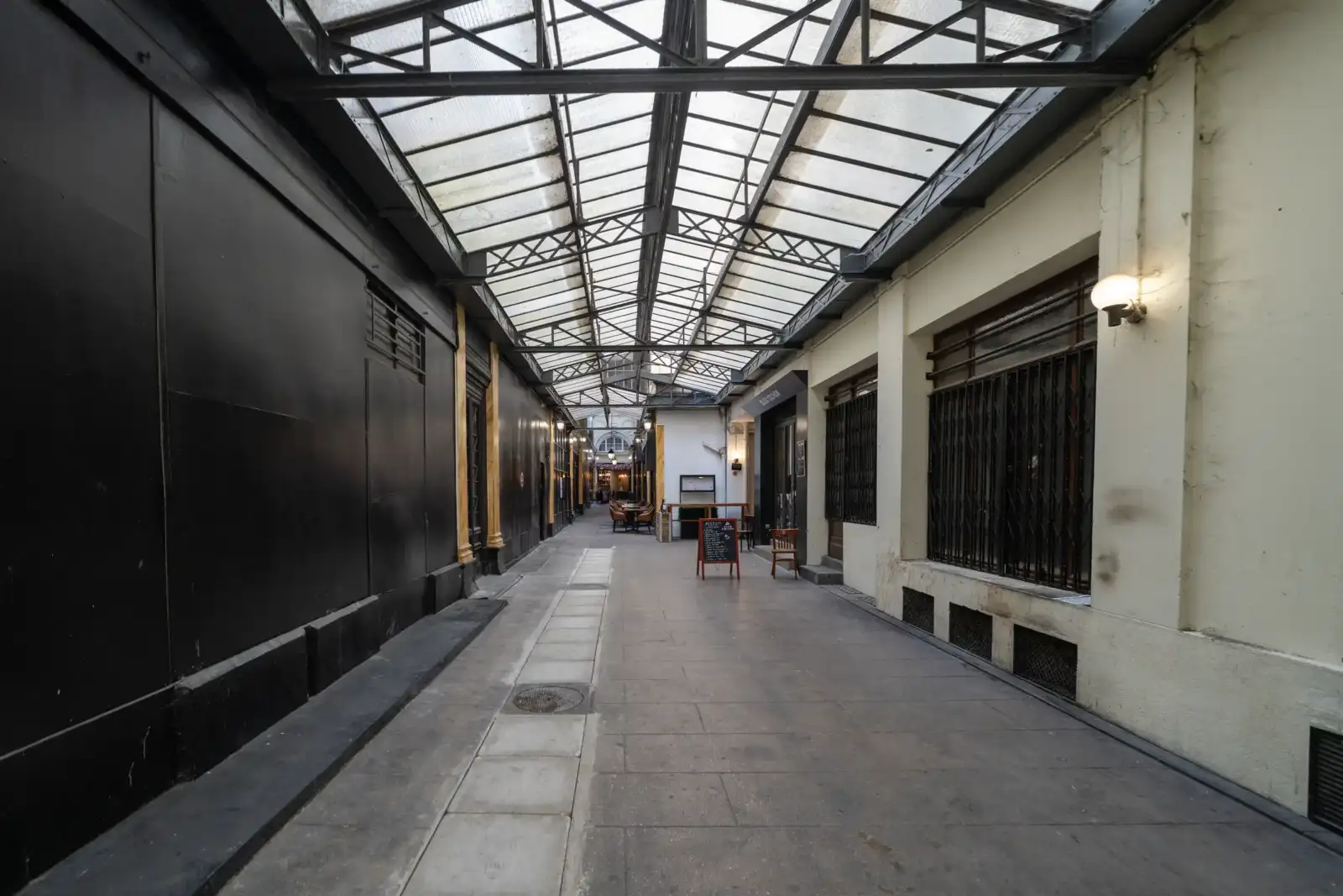 Intérieur d’un passage couvert parisien avec verrière métallique et murs contrastés.