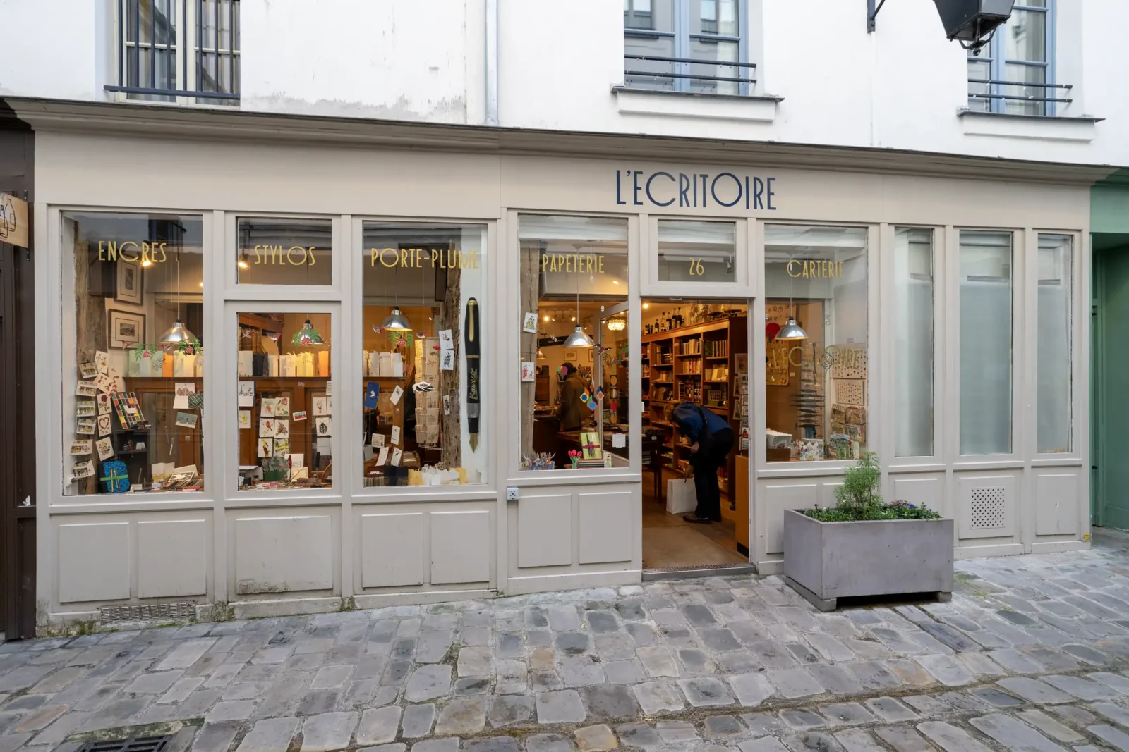La devanture beige de la boutique L'Ecritoire dans une rue pavée de Paris.