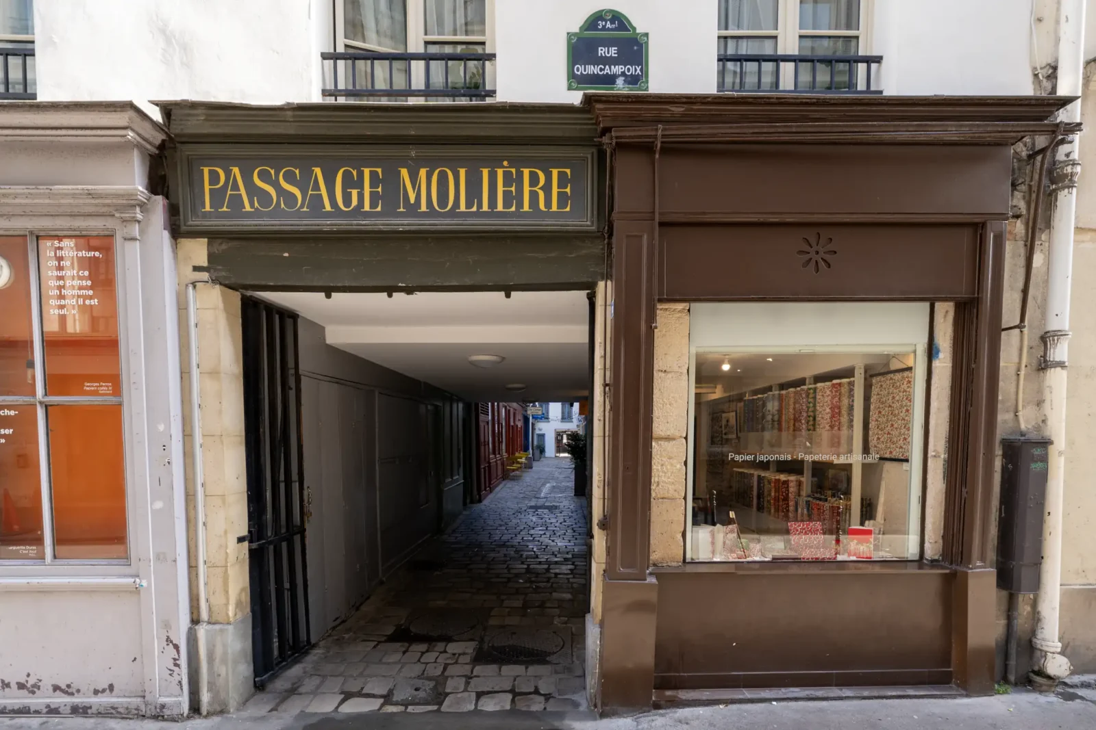 L'entrée pavée du Passage Molière à Paris avec une boutique de papier artisanal adjacente.