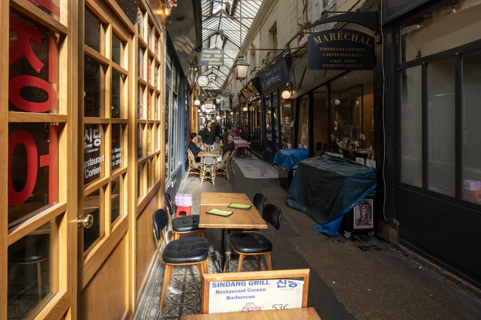 Une allée couverte parisienne avec des restaurants, des boutiques anciennes et des tables extérieures.