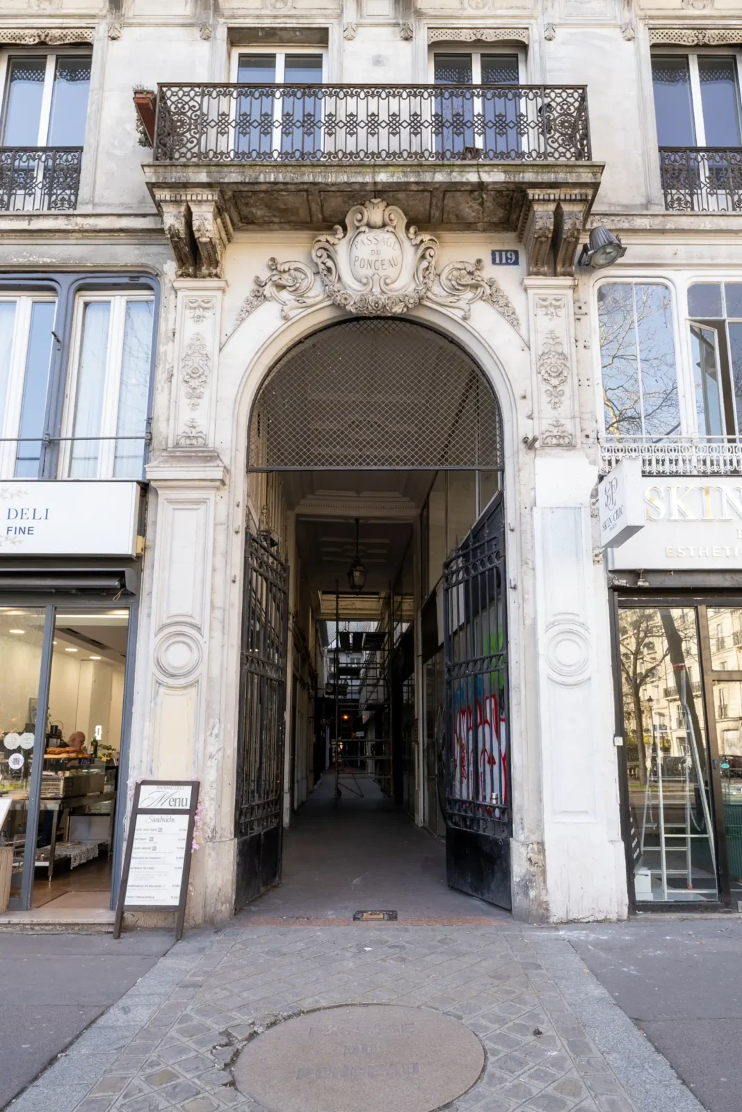 Façade historique en pierre avec une arche sculptée ouvrant sur le Passage du Ponceau.