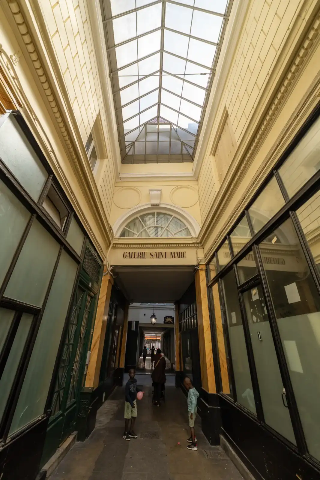 Vue en contre-plongée de la verrière et de la façade de la galerie Saint-Marc à Paris.
