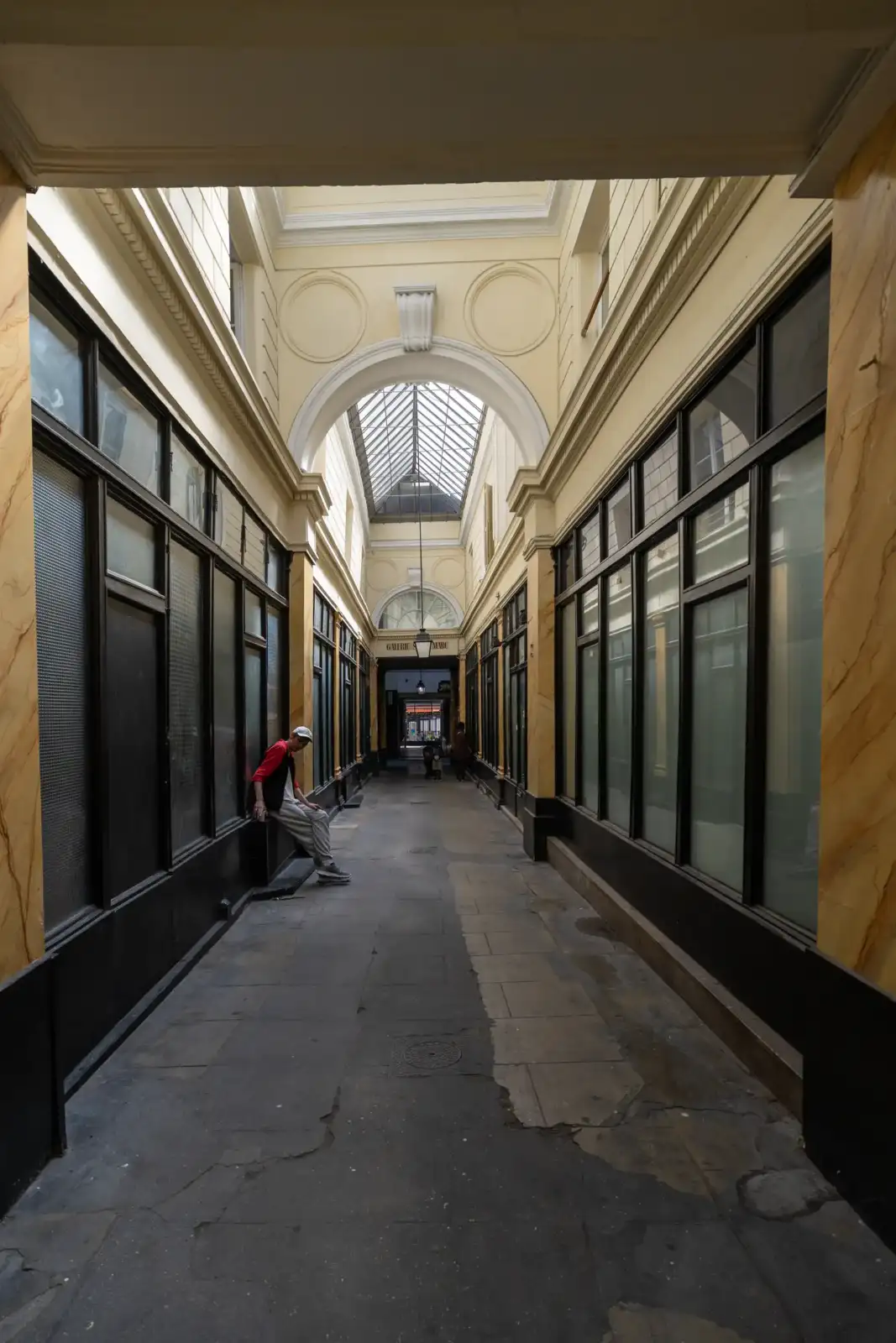 Un homme est assis dans le Passage Saint Marc à Paris sous une verrière.