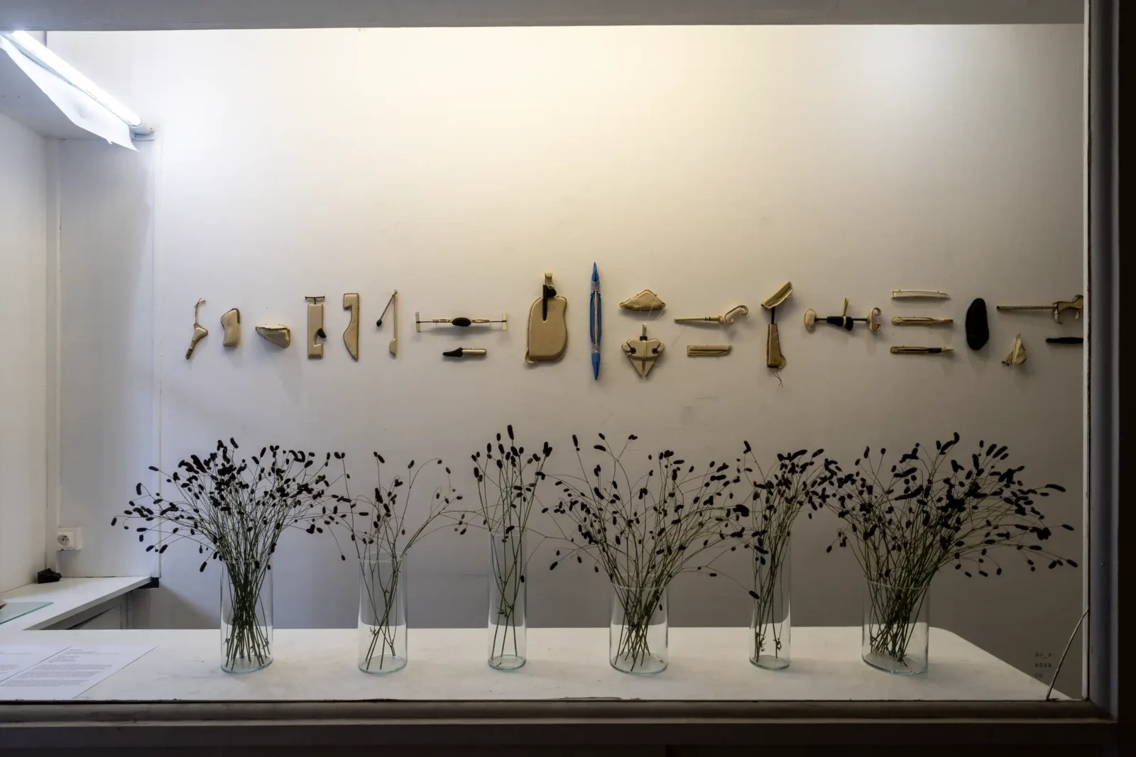 Des objets dorés sont exposés au mur au-dessus de six vases remplis de fleurs.