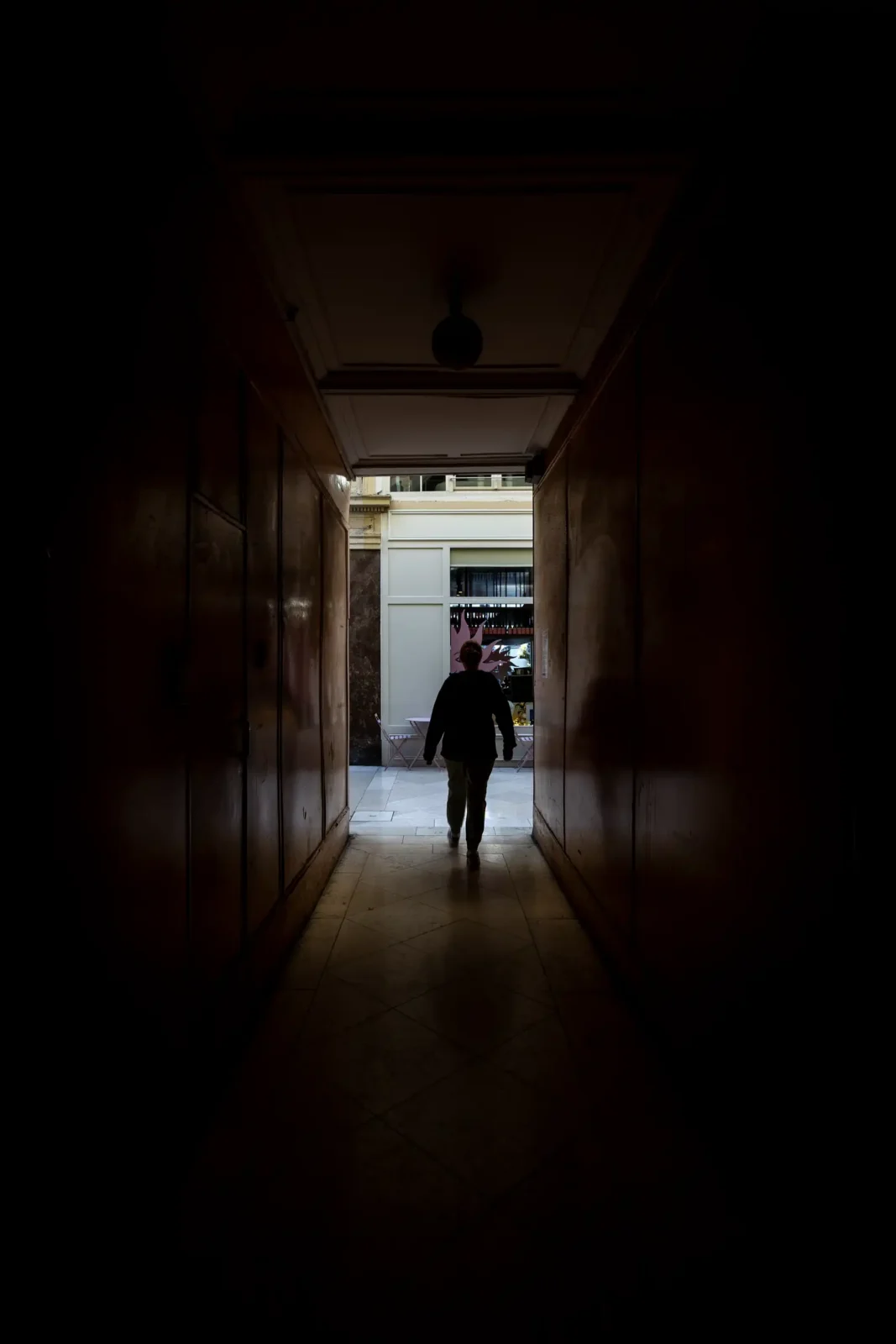 Une silhouette marche dans un passage sombre vers une sortie lumineuse à Paris.