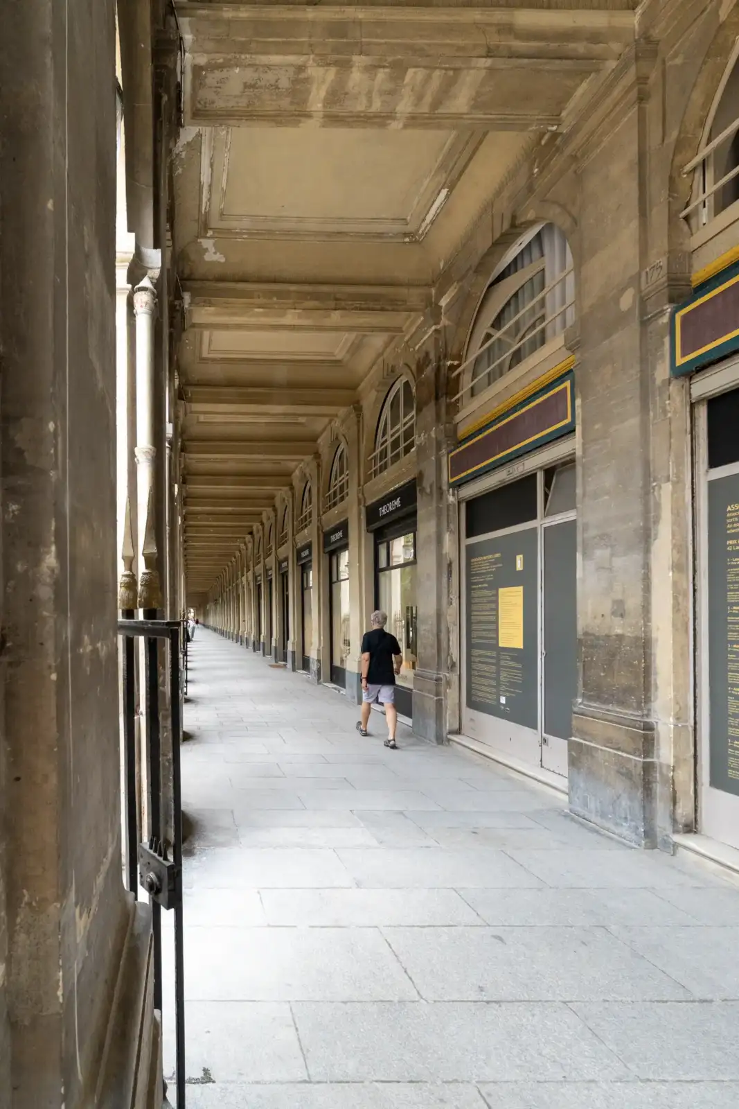 Une personne solitaire marche sous les arcades voûtées du passage Valois à Paris.