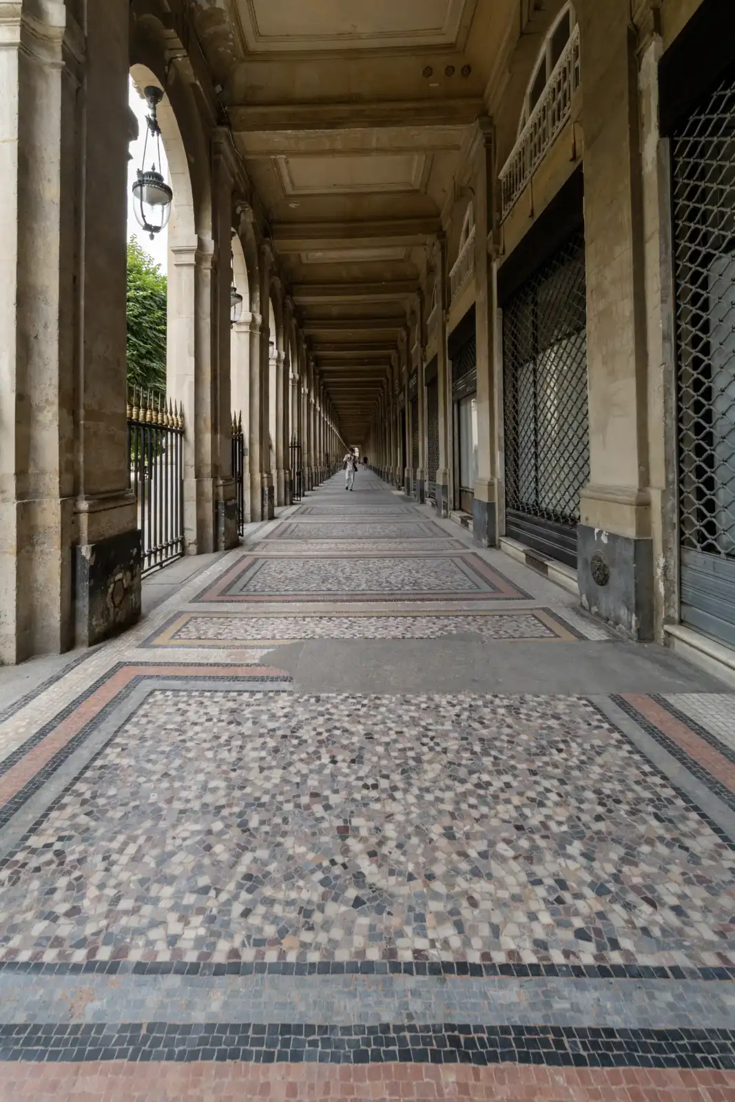 Vue en perspective d'une longue galerie couverte aux sols en mosaïque géométrique à Paris.
